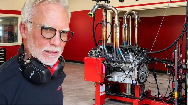 Dave Bell in ear defenders beside a V12 engine on a test stand in the red shop
