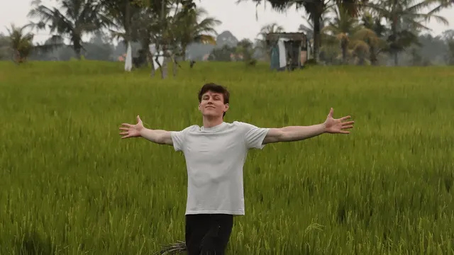 Jon Law standing with arms wide in a green rice field